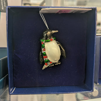 Penguin ornament with a red and green bow tie in a blue box on a glass surface.